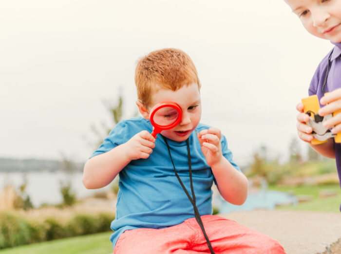 Young child using a bright red magnifying glass to examine something small.